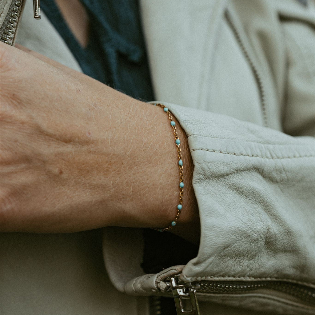 Close-up of a person wearing a beige jacket with a brown leather bracelet and permanent bracelet.