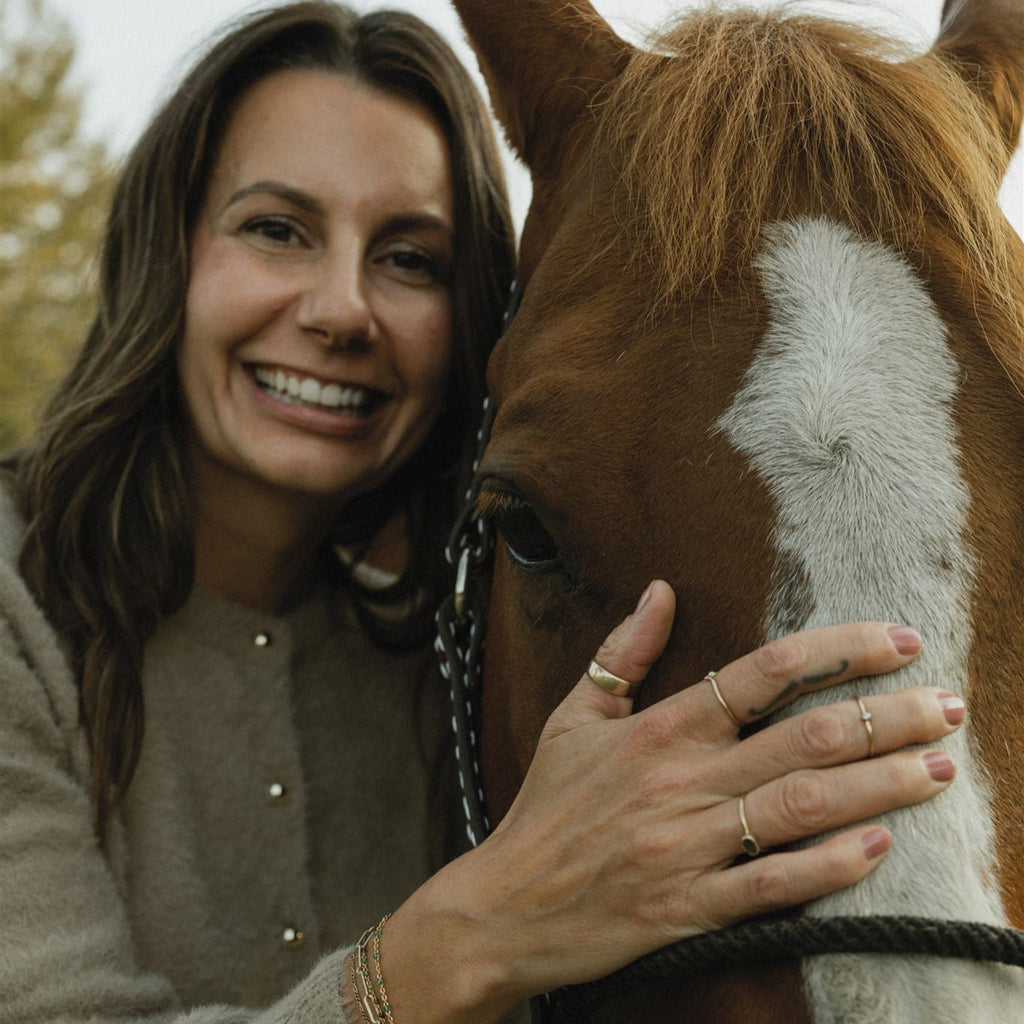 Woman smiling and petting a brown and white horse outdoors.