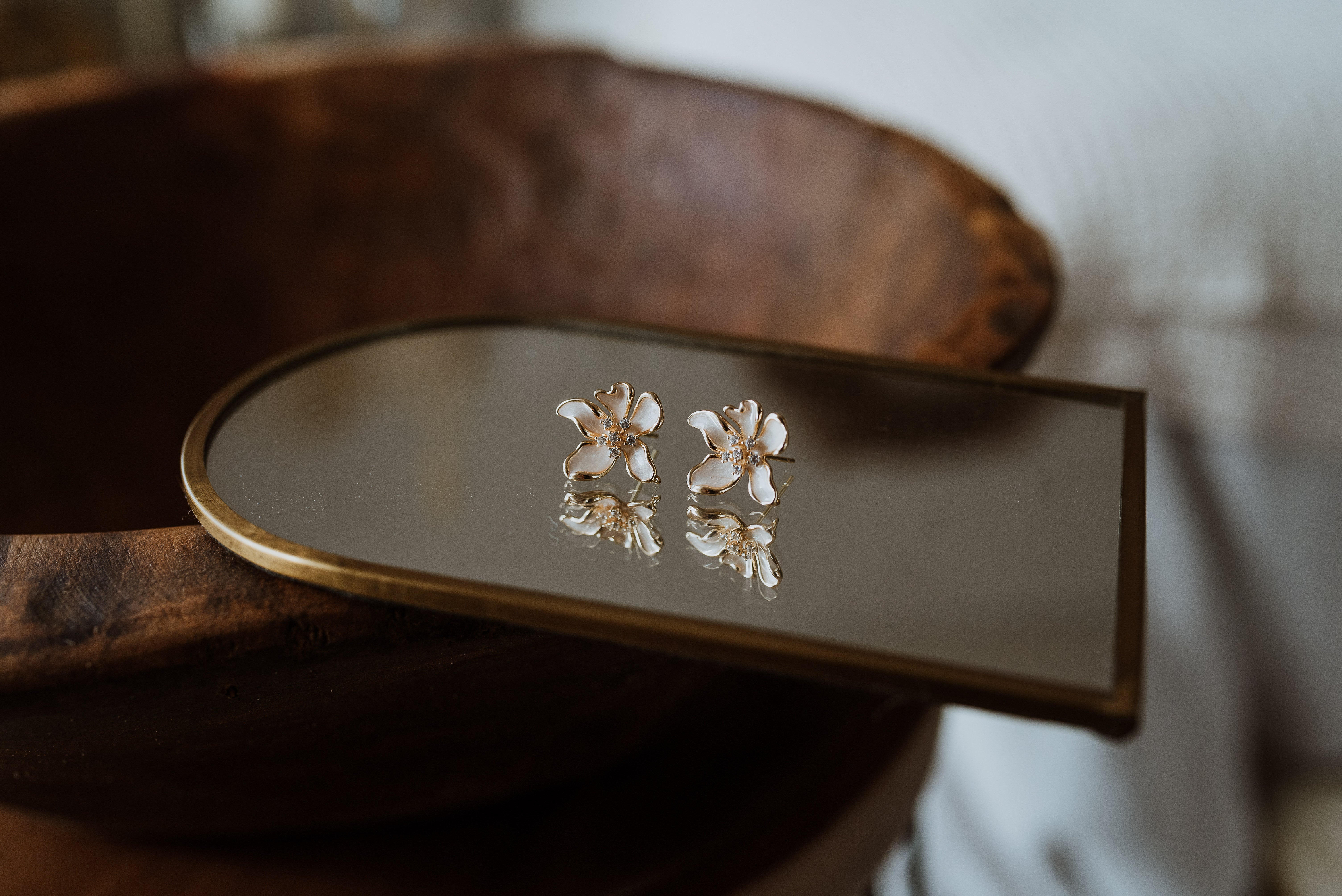 Floral earrings on a reflective surface with a wooden background