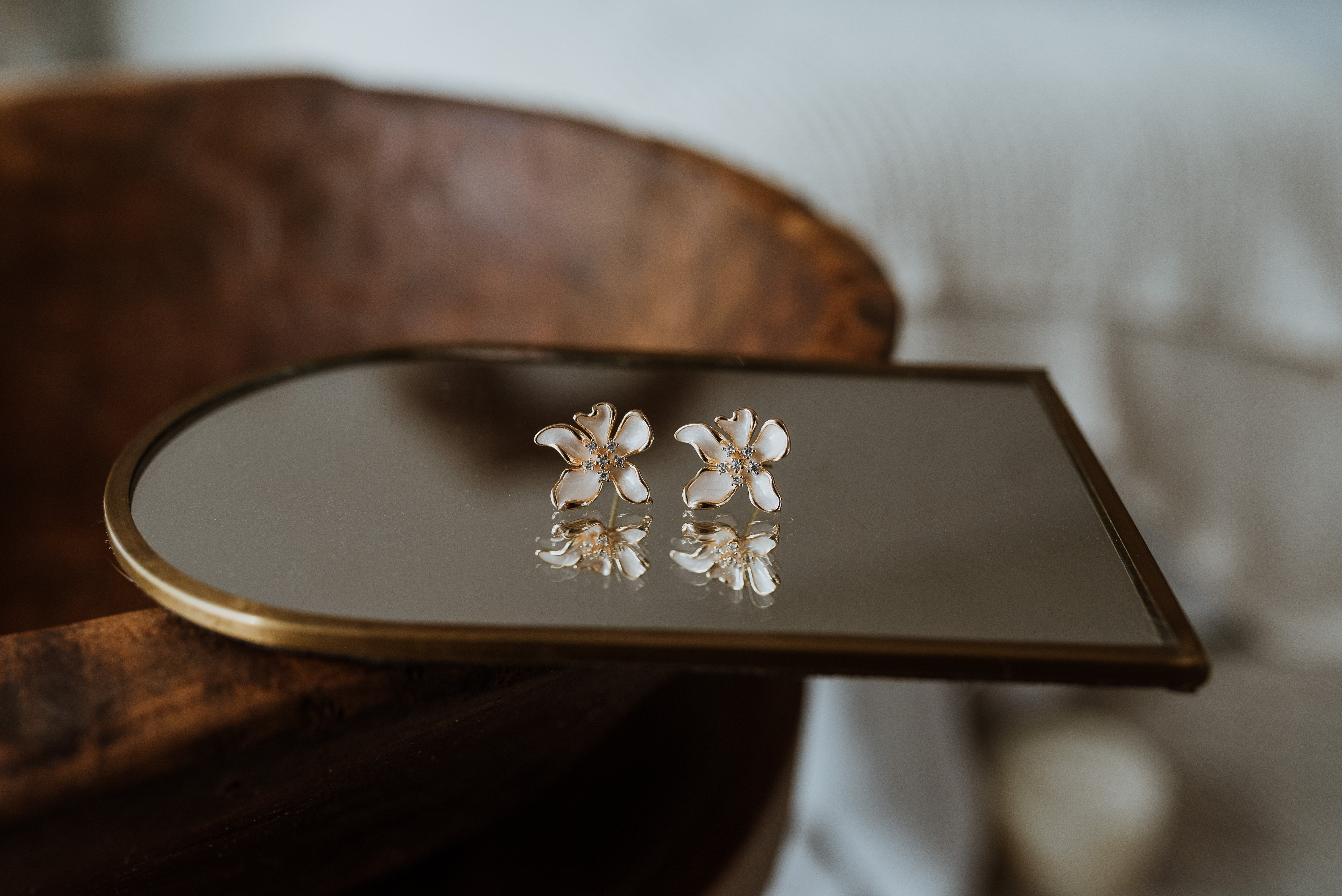 Pair of floral earrings on a reflective surface with a blurred background