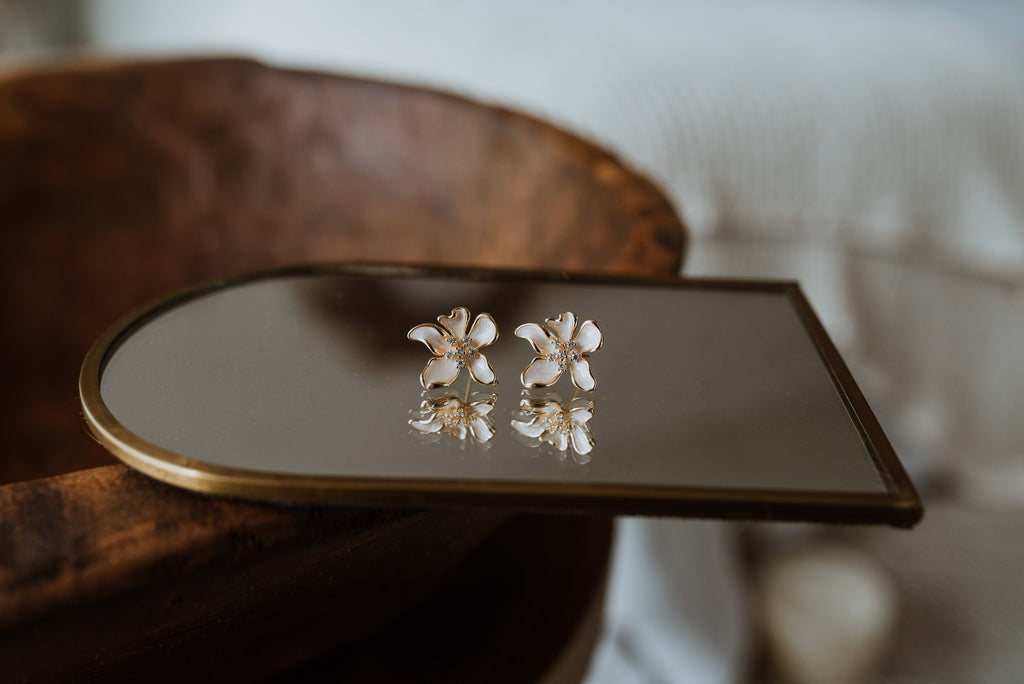 Pair of floral earrings on a reflective surface with a blurred background