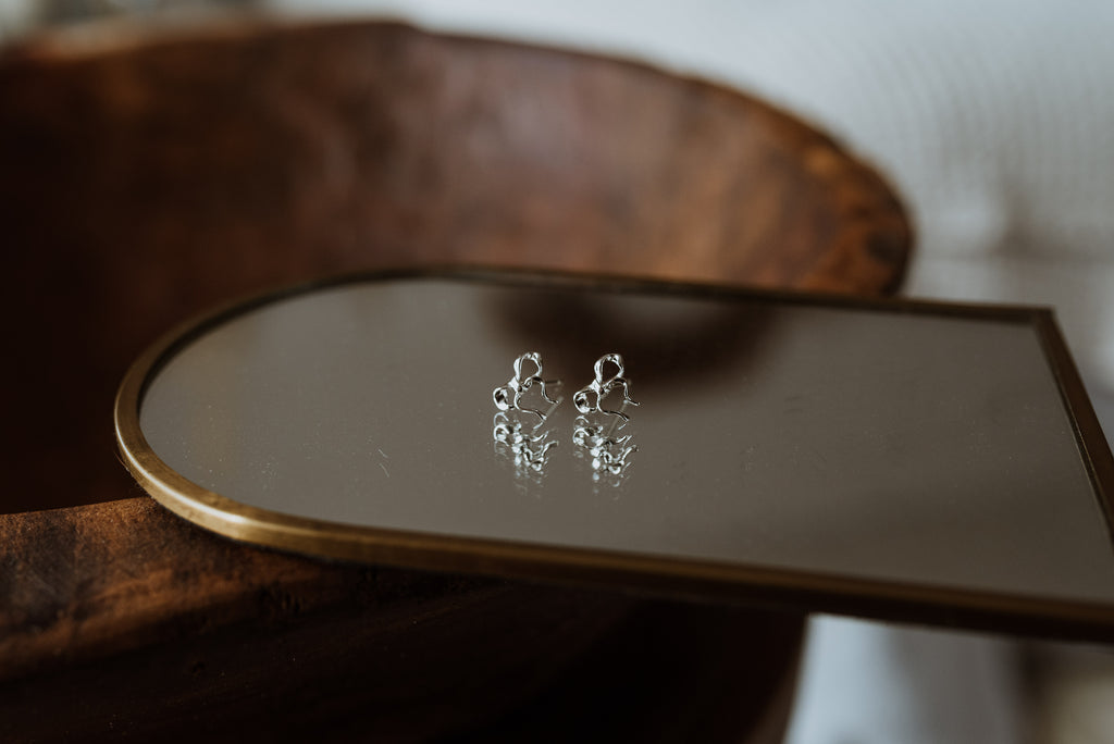 Silver earrings on a reflective surface with a wooden background
