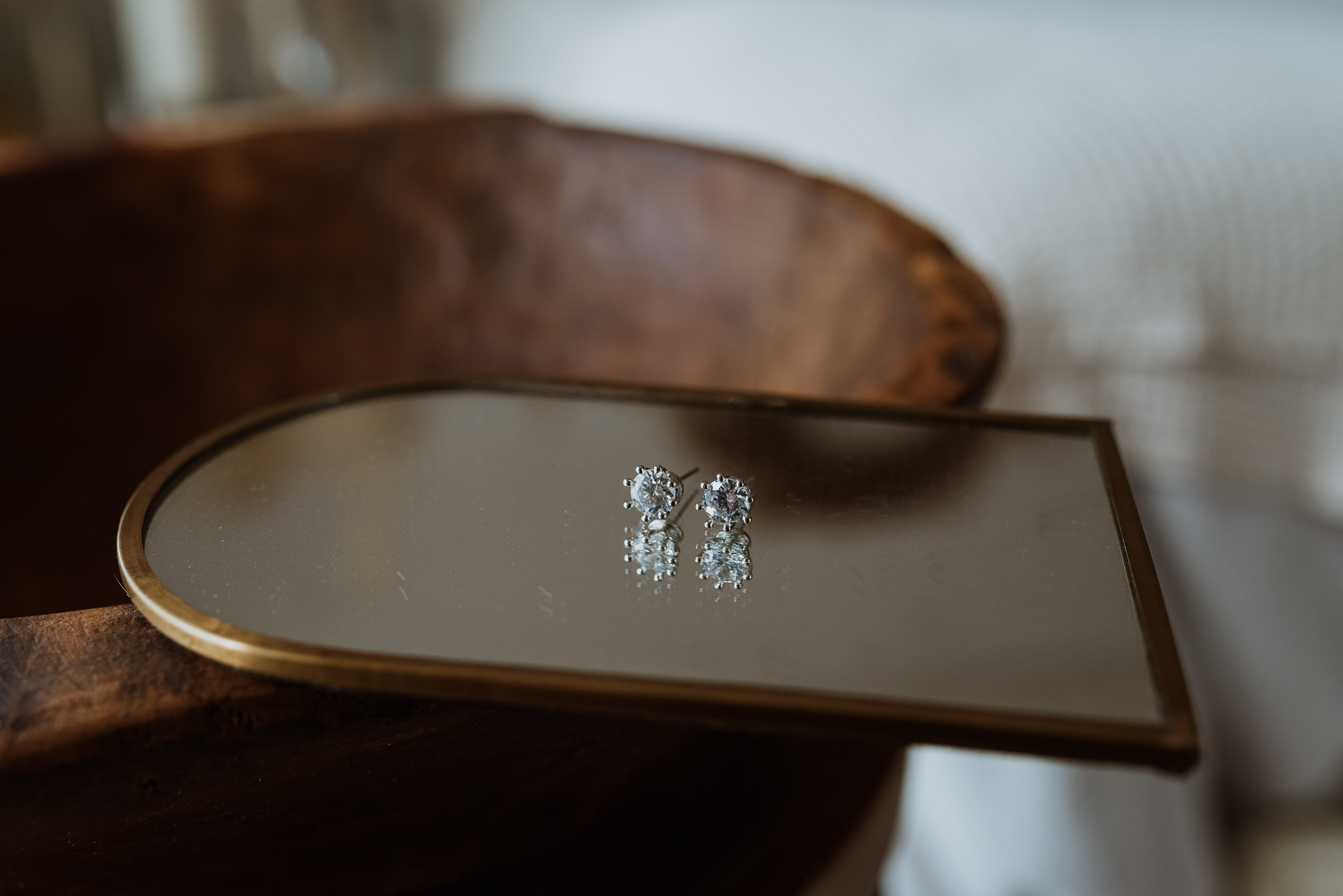 Pair of earrings on a reflective surface with a wooden background