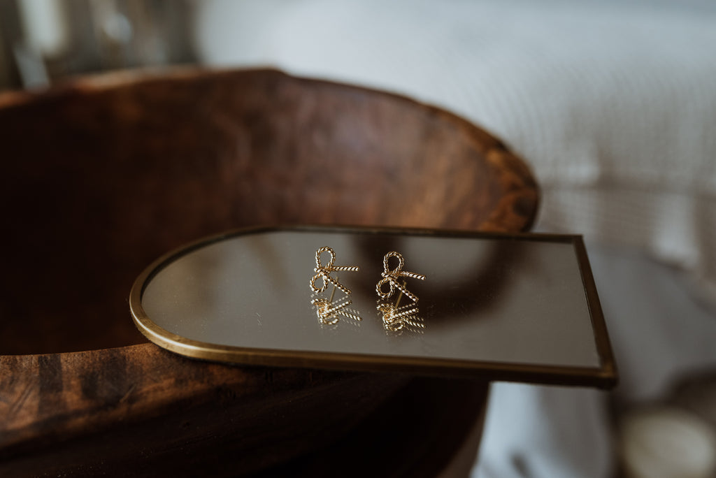 Gold earrings on a small mirror with a wooden surface