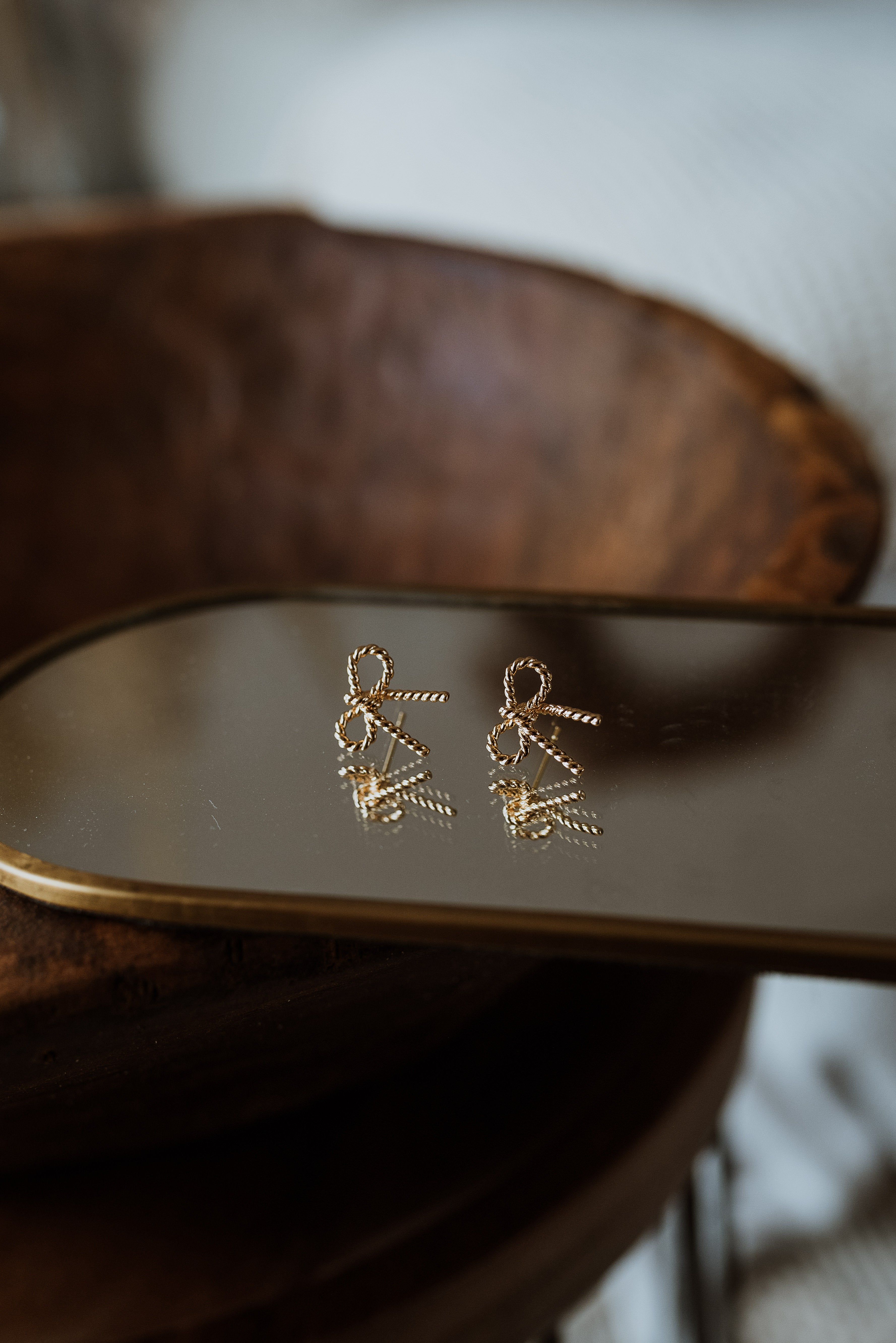 Gold earrings on a reflective surface with a wooden background