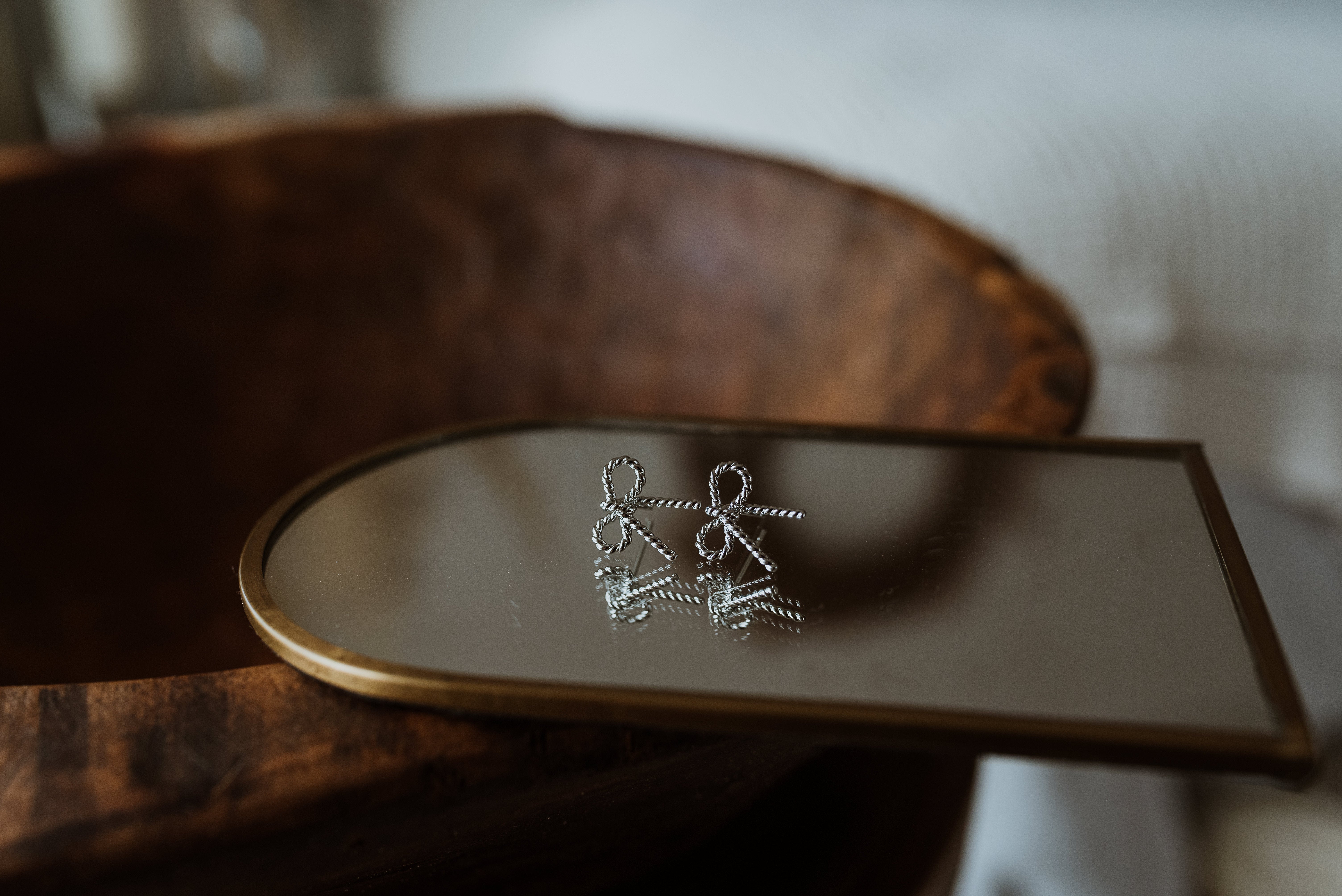 Pair of silver earrings on a reflective surface with a wooden background