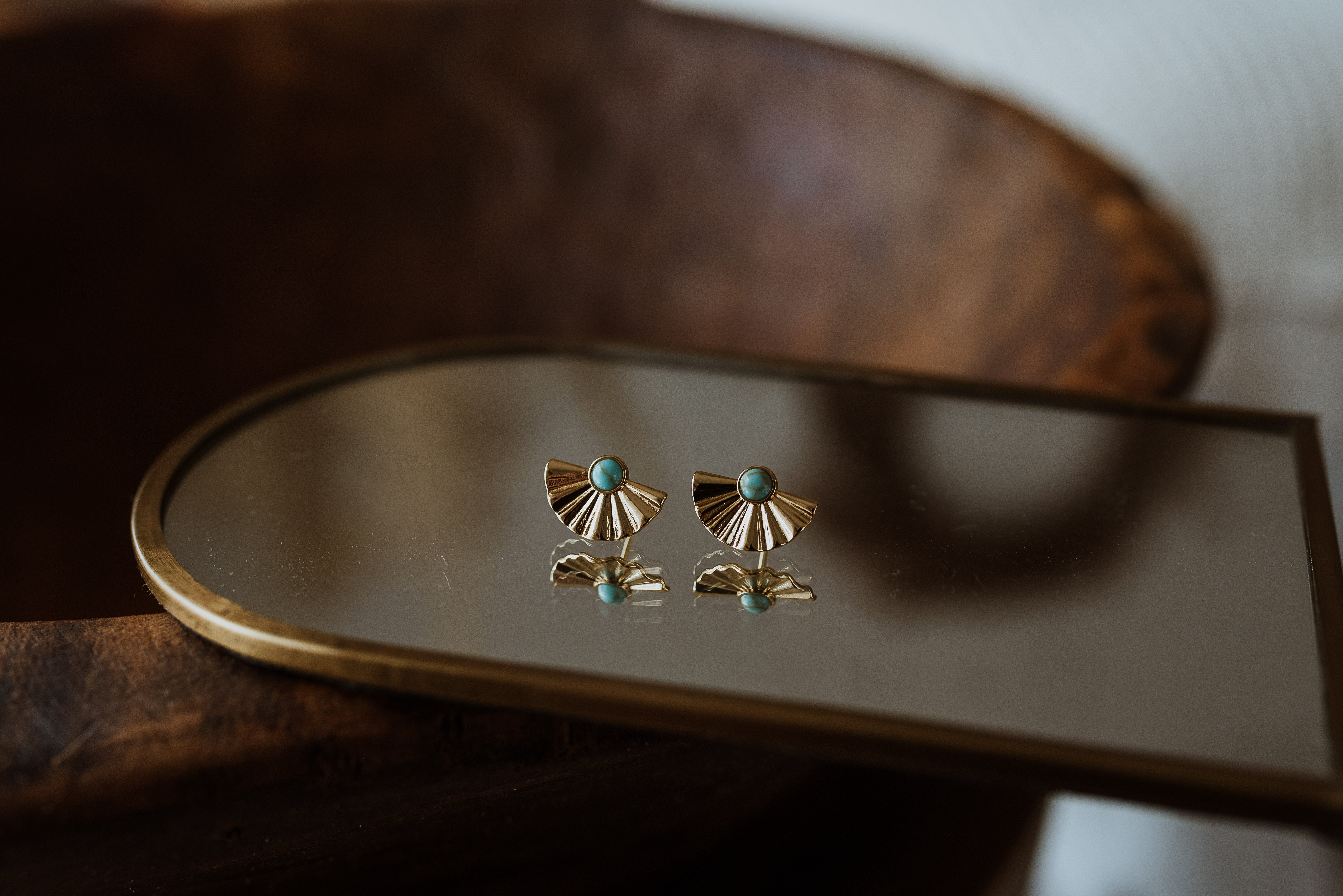 Pair of gold earrings with turquoise stones on a mirror surface