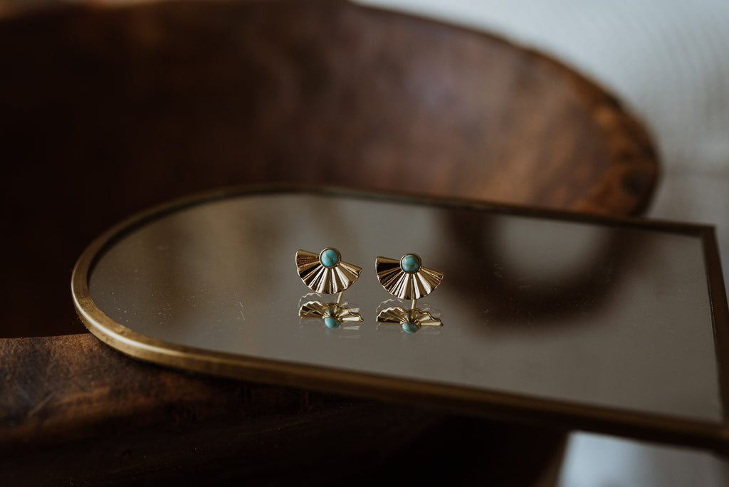 Pair of gold earrings with turquoise stones on a mirror surface