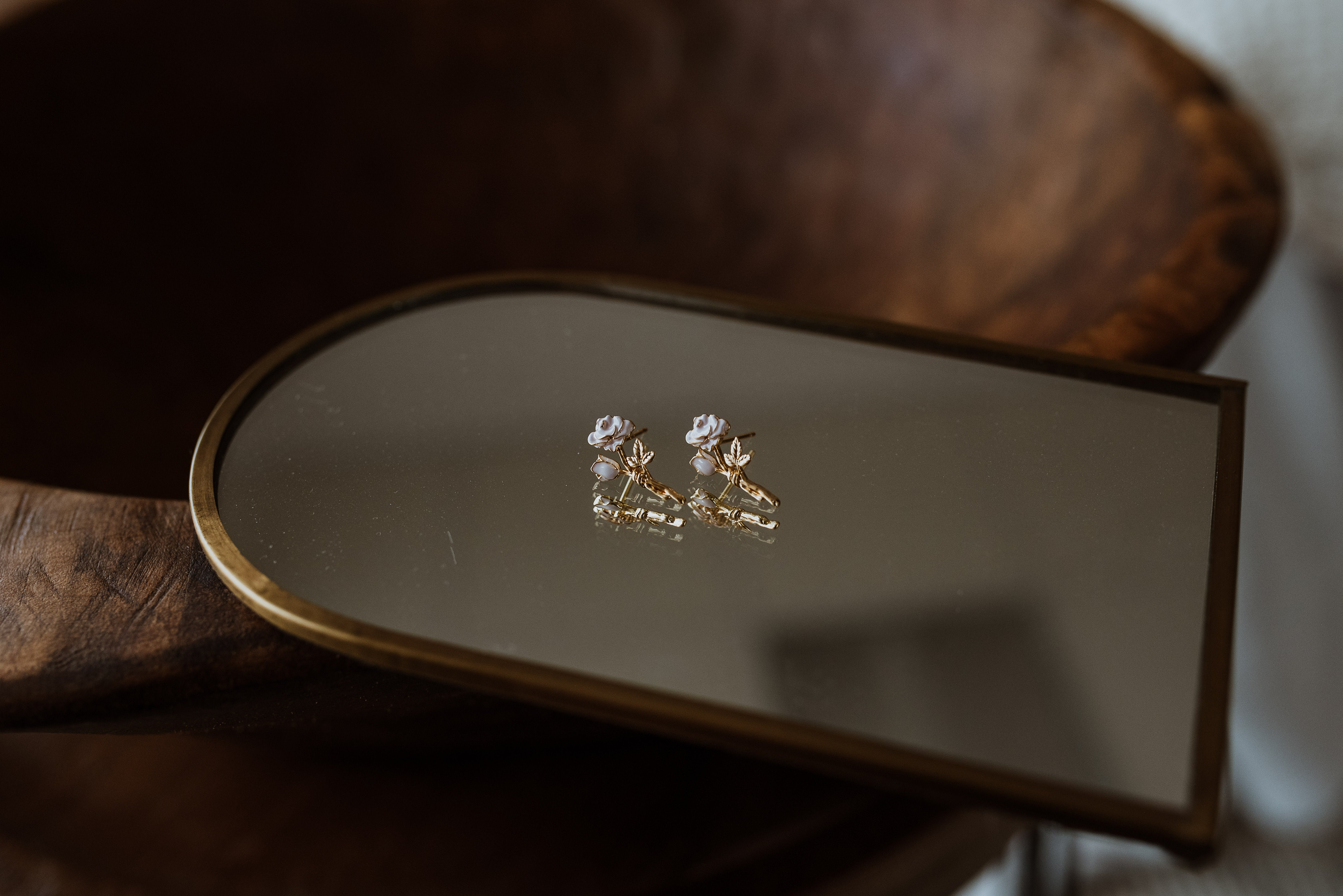 Pair of rose earrings on a reflective surface with a wooden background