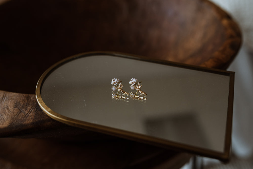 Pair of rose earrings on a reflective surface with a wooden background