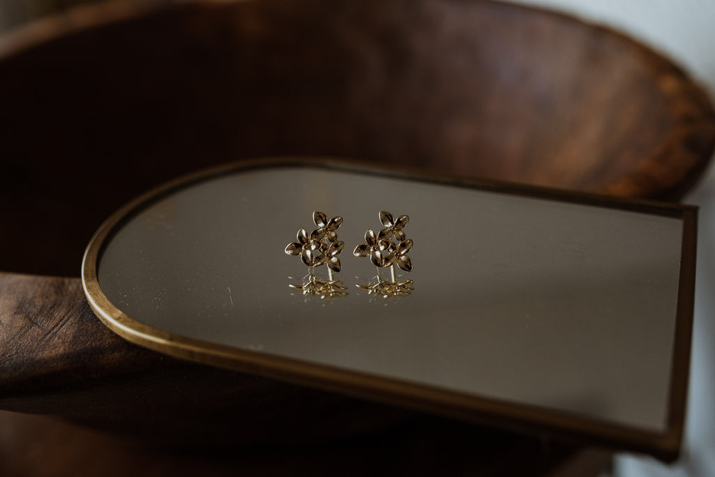 Gold earrings on a reflective surface with a wooden background