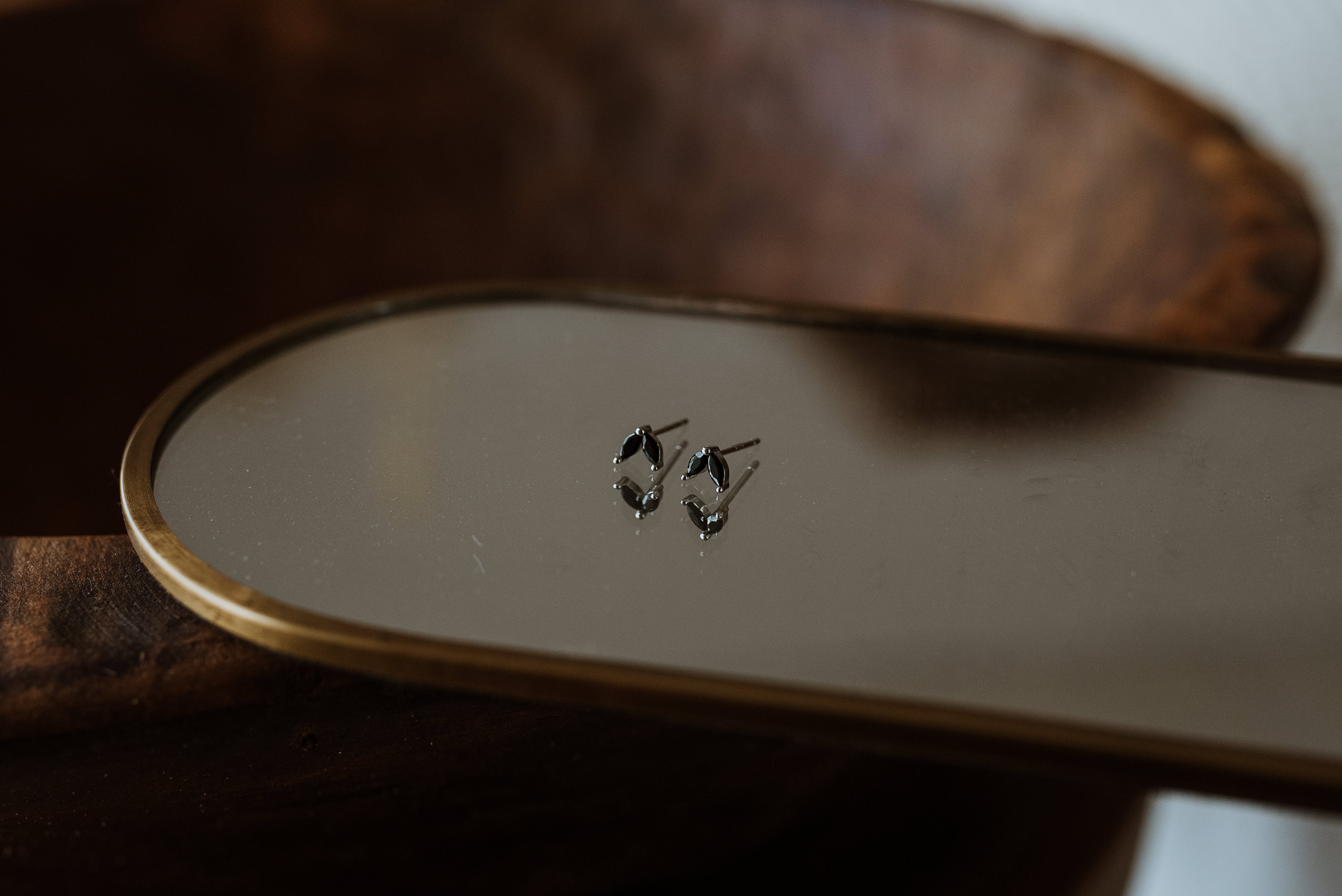 Pair of black earrings on a mirror with a wooden surface in the background