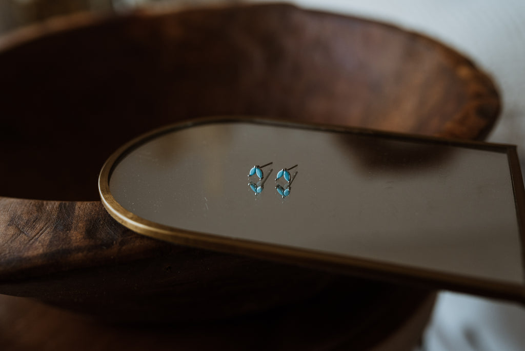 Pair of turquoise earrings on a wooden surface with a mirror reflection.
