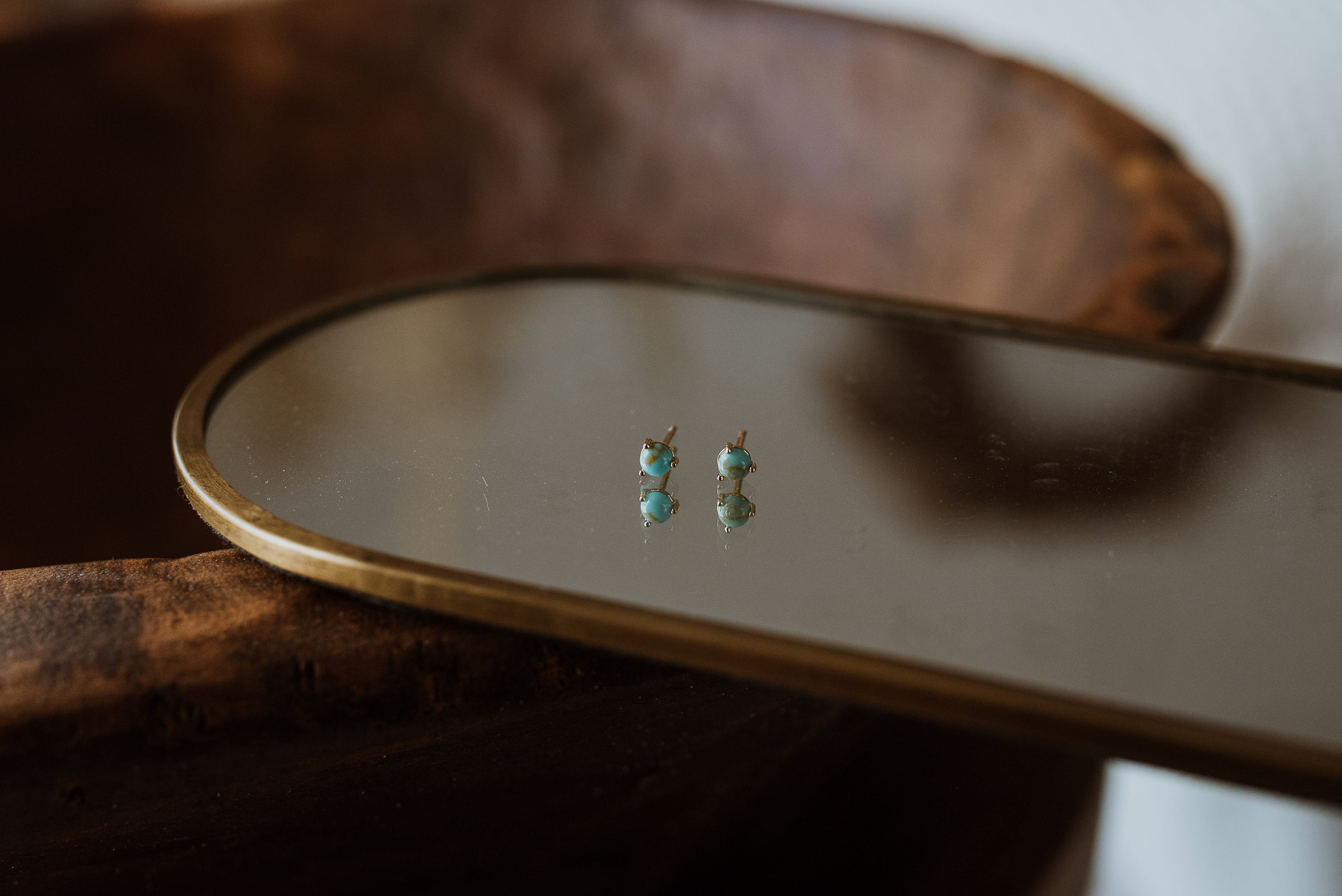 Pair of turquoise earrings on a small mirror with a wooden base