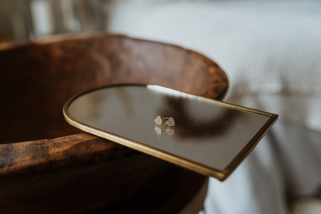 Heart-shaped earrings on a mirror with gold frame on a wooden surface