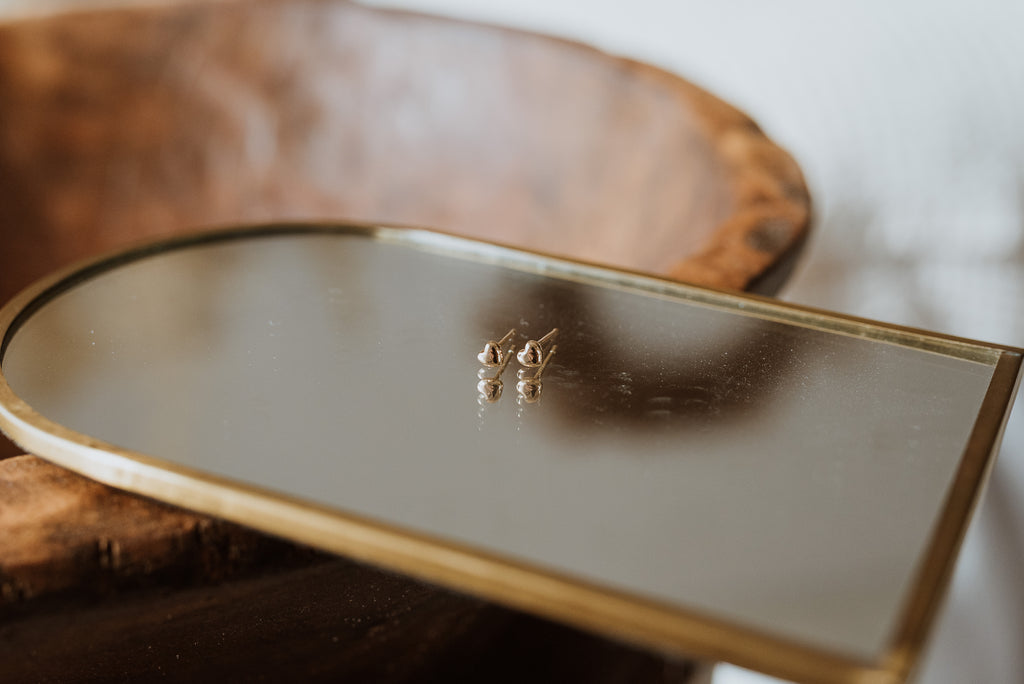 Gold earrings on a reflective surface with a wooden background
