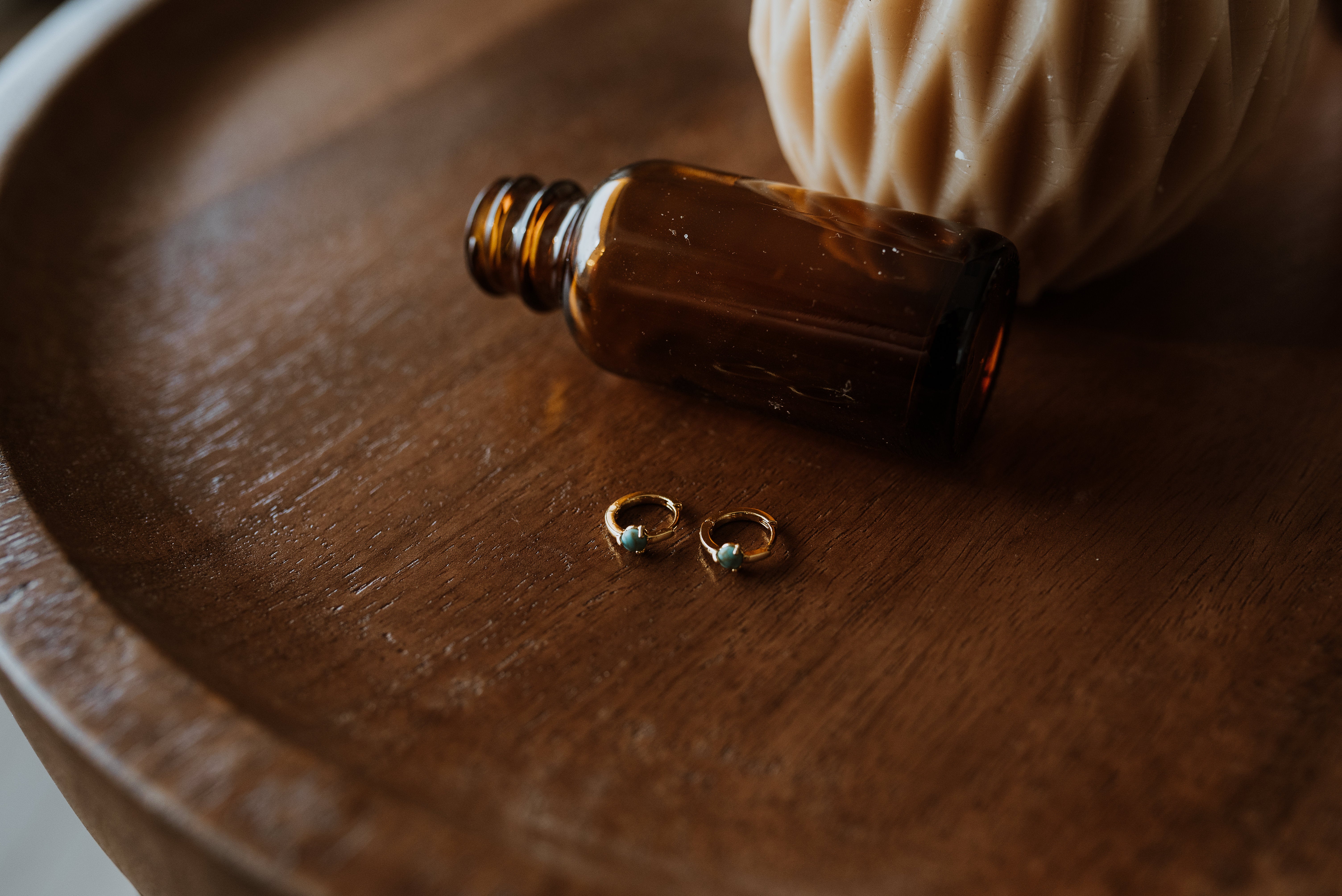 Small brown bottle with gold earrings on a wooden surface
