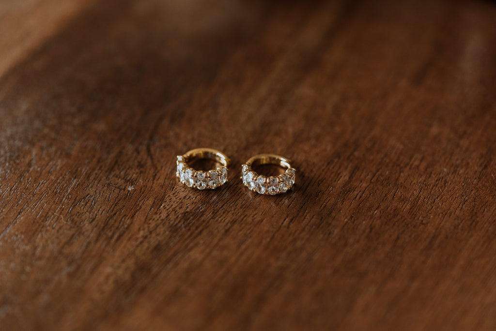 Pair of gold hoop earrings with embedded stones on a wooden surface