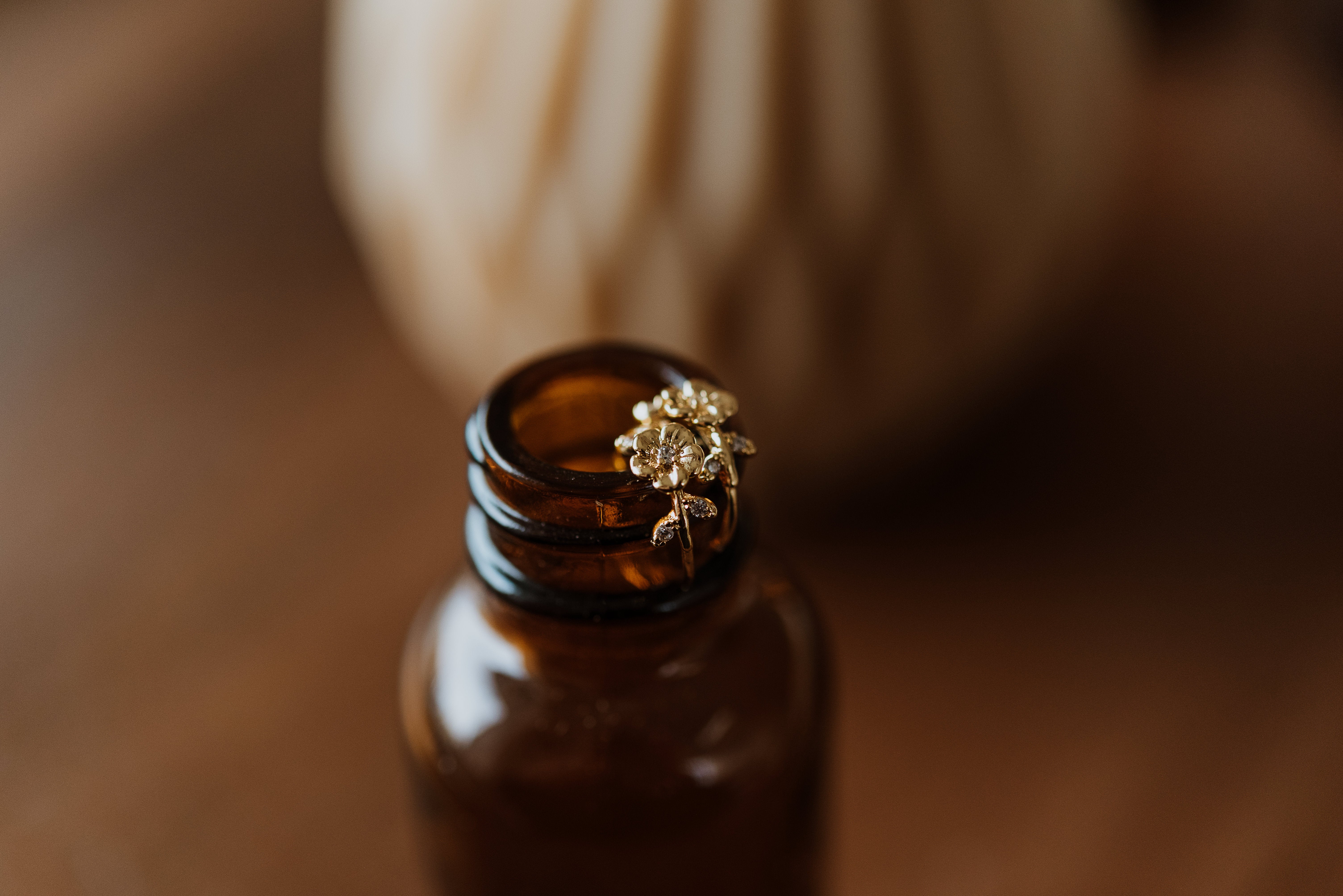 Gold earring with floral design on top of a brown glass bottle against a blurred background