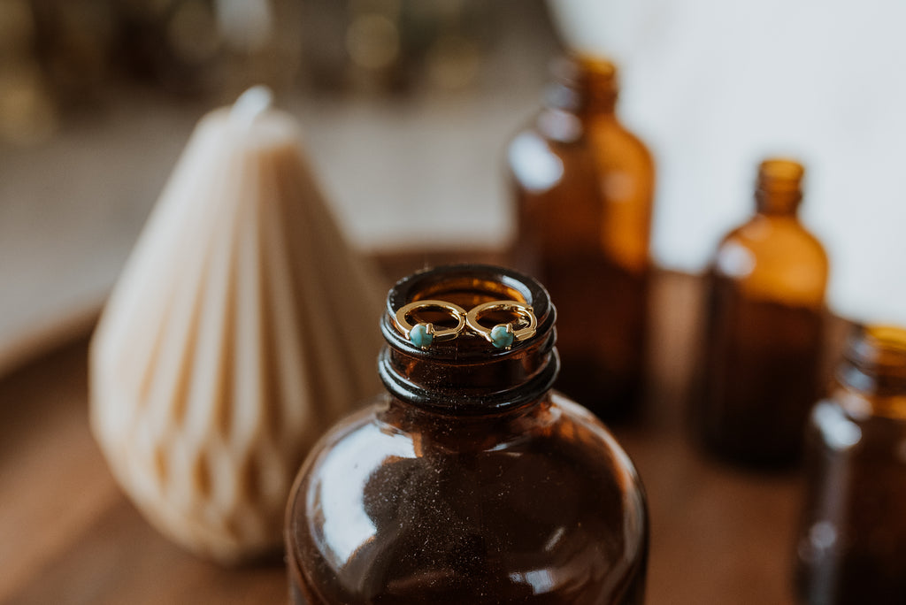 Brown glass bottle with earrings on top, surrounded by other similar bottles and a candle.
