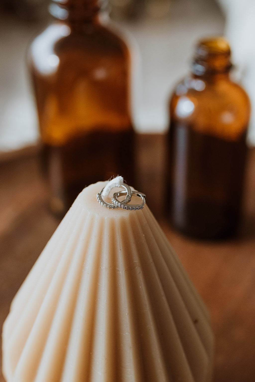 Earrings on a candle with two amber bottles in the background