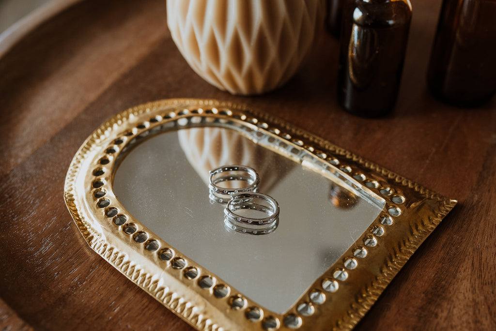 Two earrings on a heart-shaped mirror with decorative gold frame on a wooden surface.