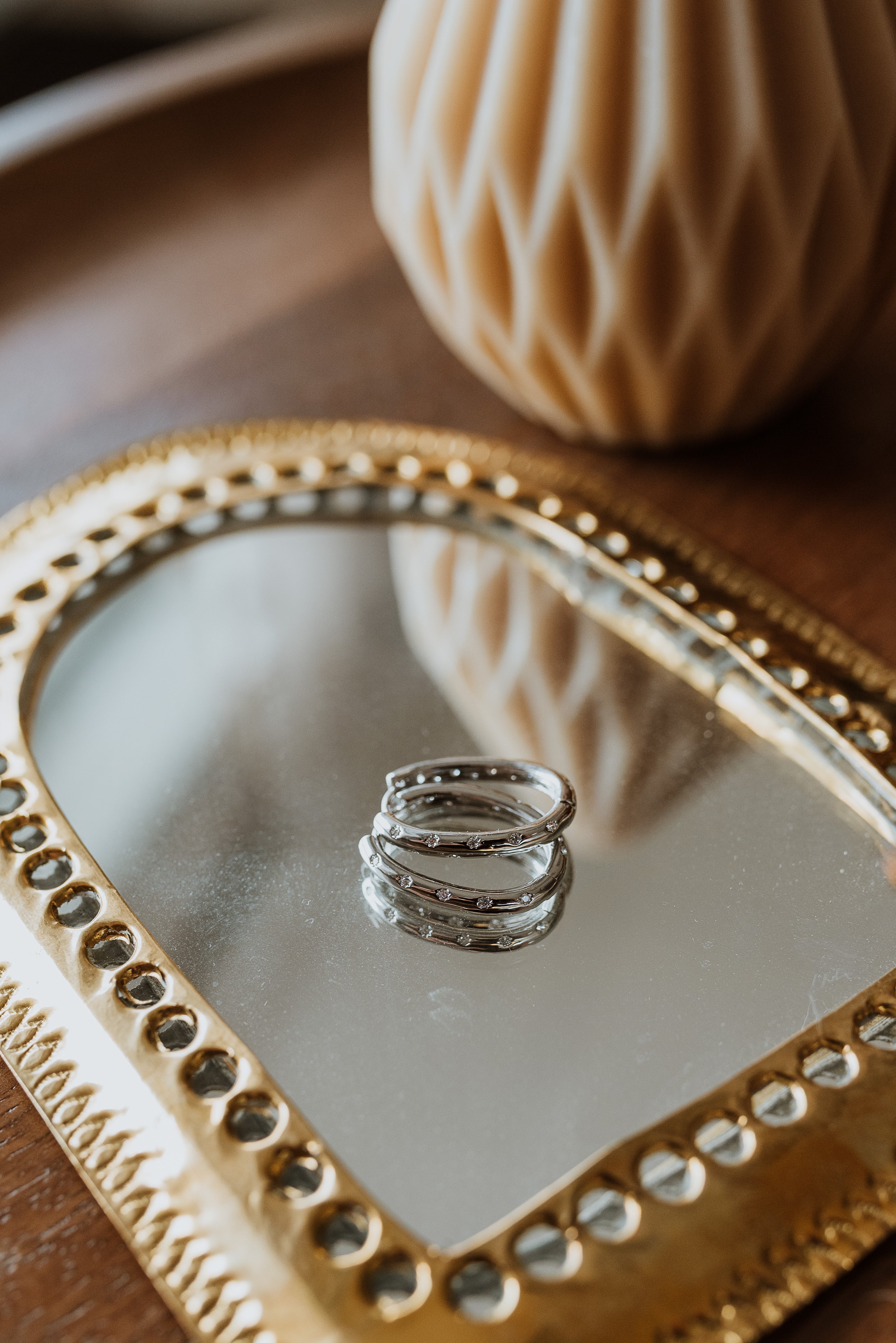 Two silver earrings on a heart-shaped mirror with a textured beige object in the background