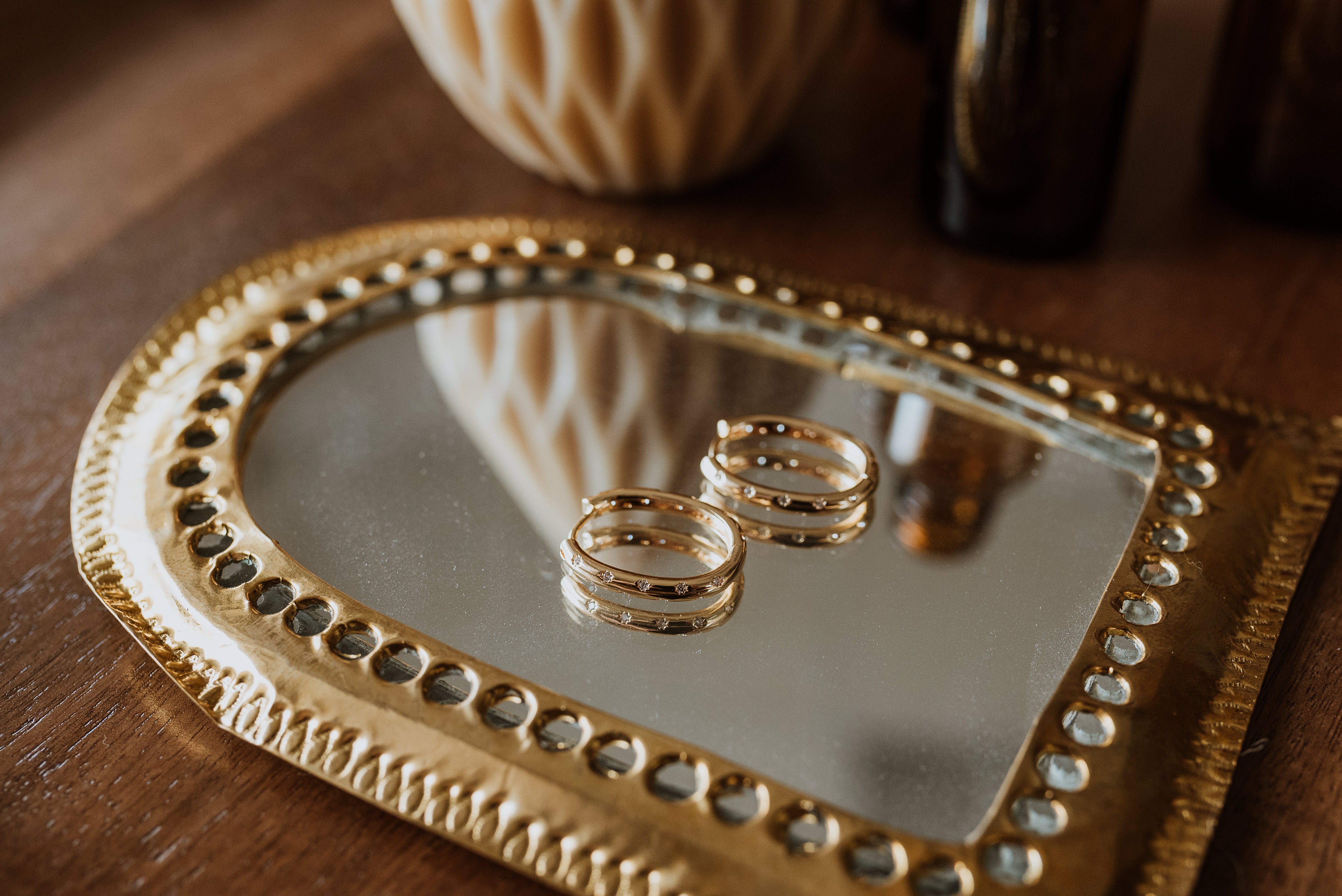 Gold earrings on a heart-shaped mirror with a decorative gold frame on a wooden surface.