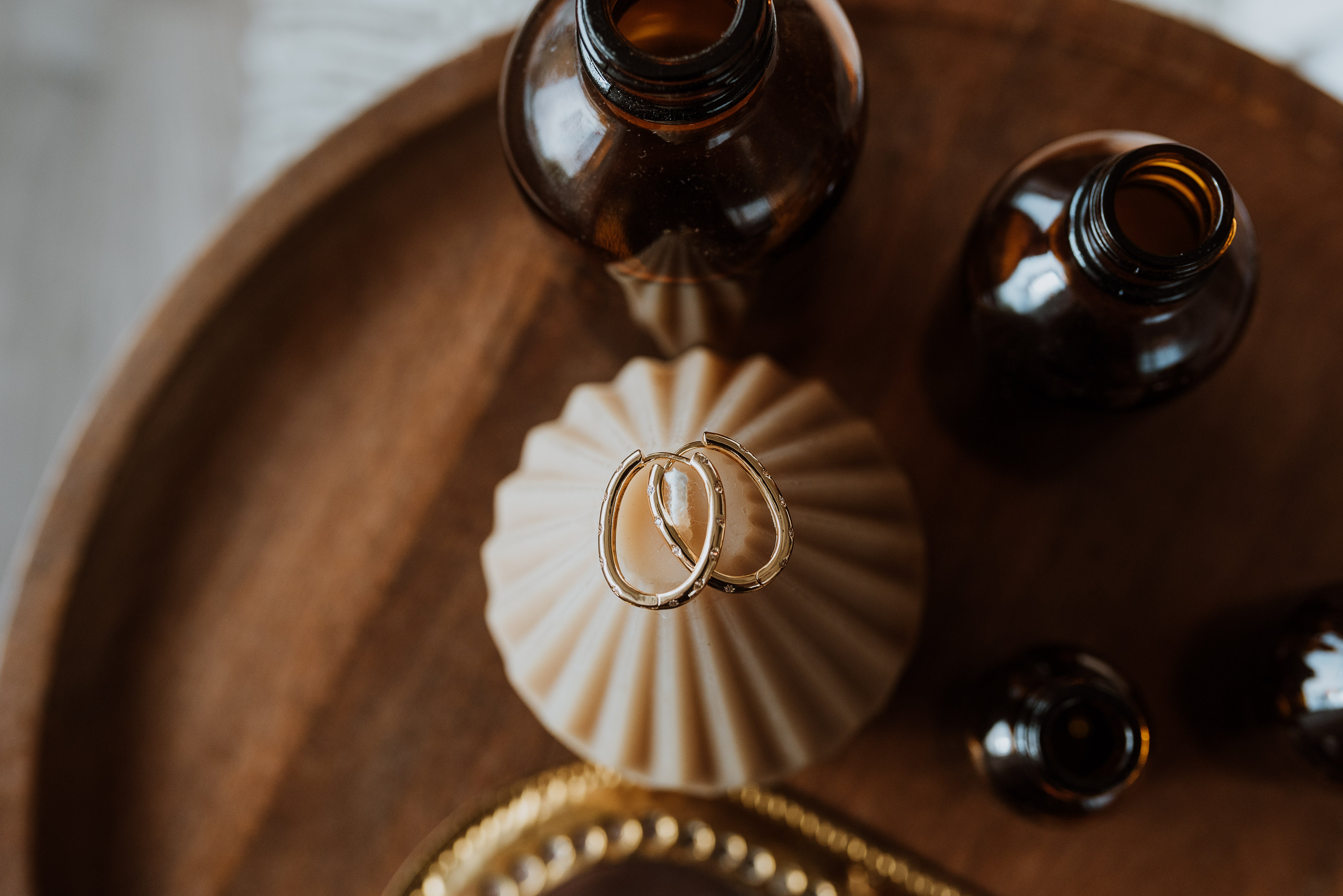 Two gold earrings on a wooden tray with two brown bottles.