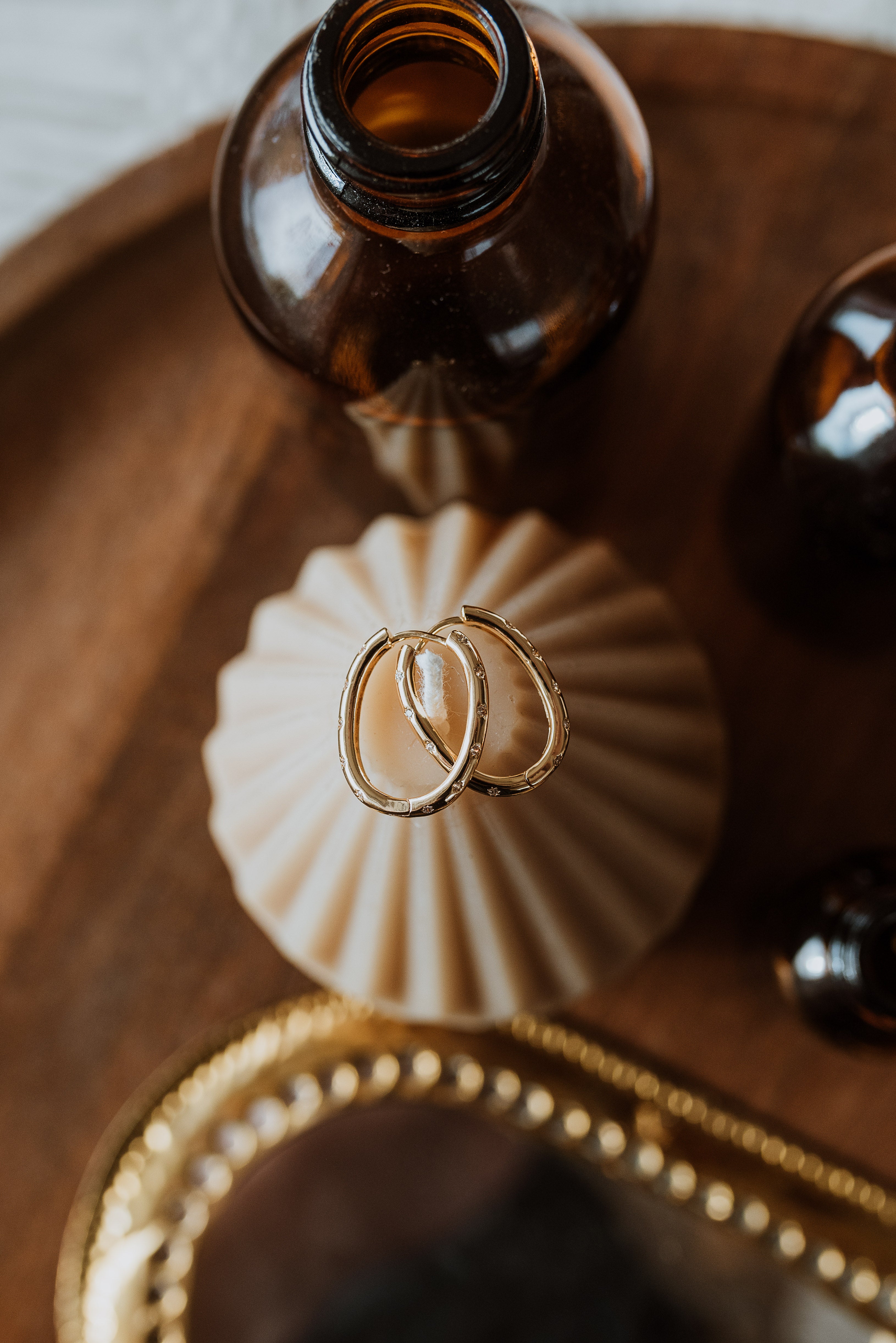 Gold earrings on a decorative candle with brown bottles in the background