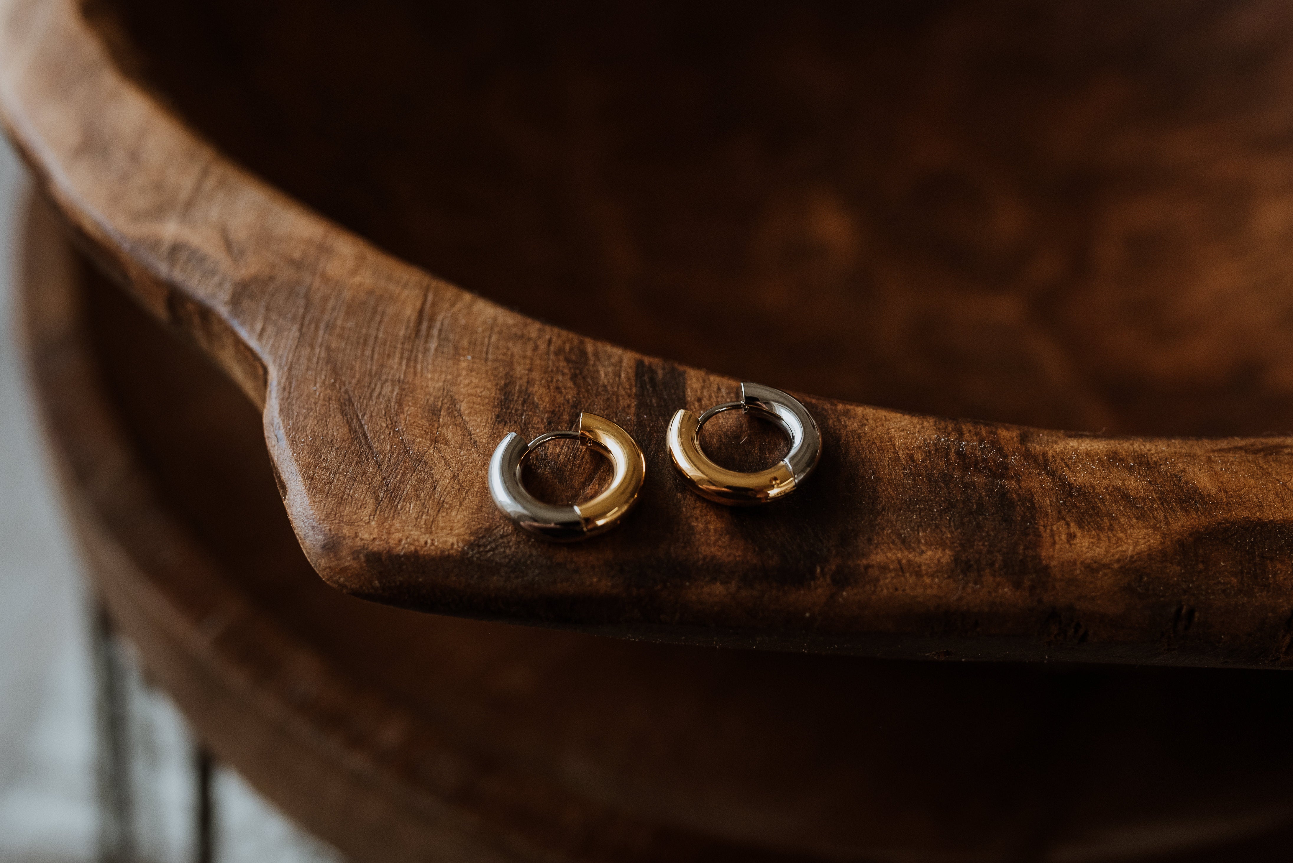 Two gold and silver hoop earrings on a wooden surface