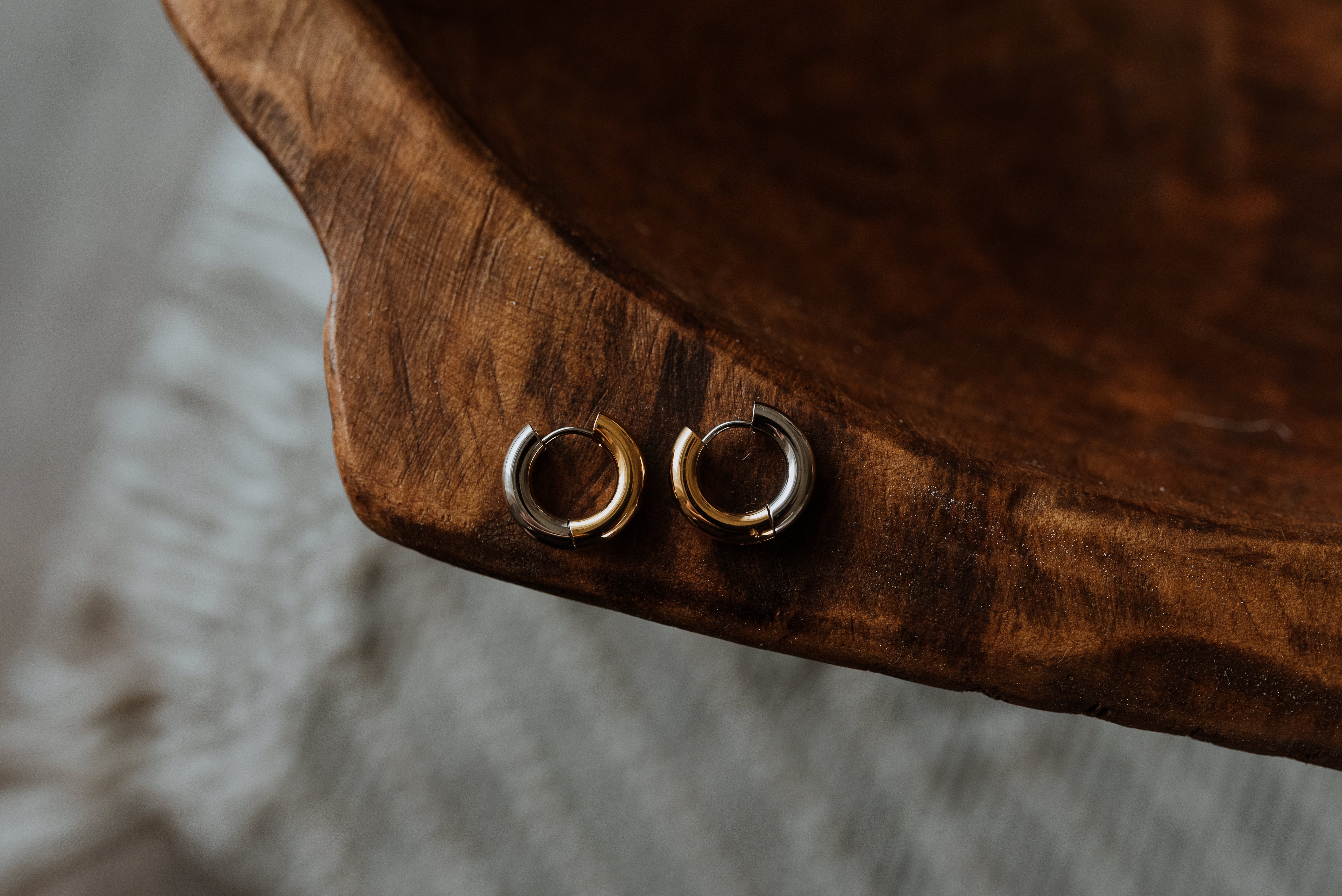 Pair of silver and gold hoop earrings on a wooden surface with a blurred background