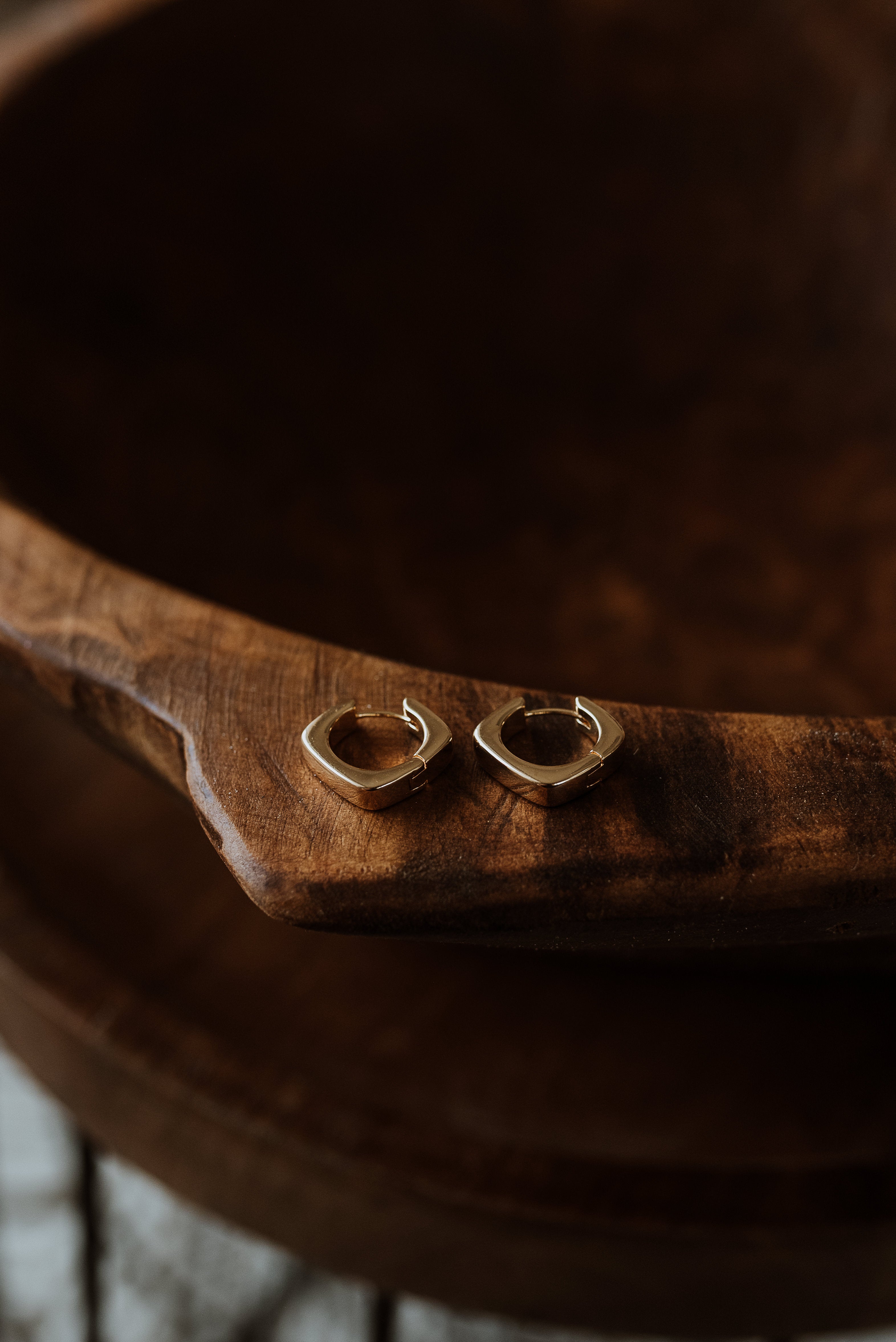 Gold square hoop earrings on a wooden surface