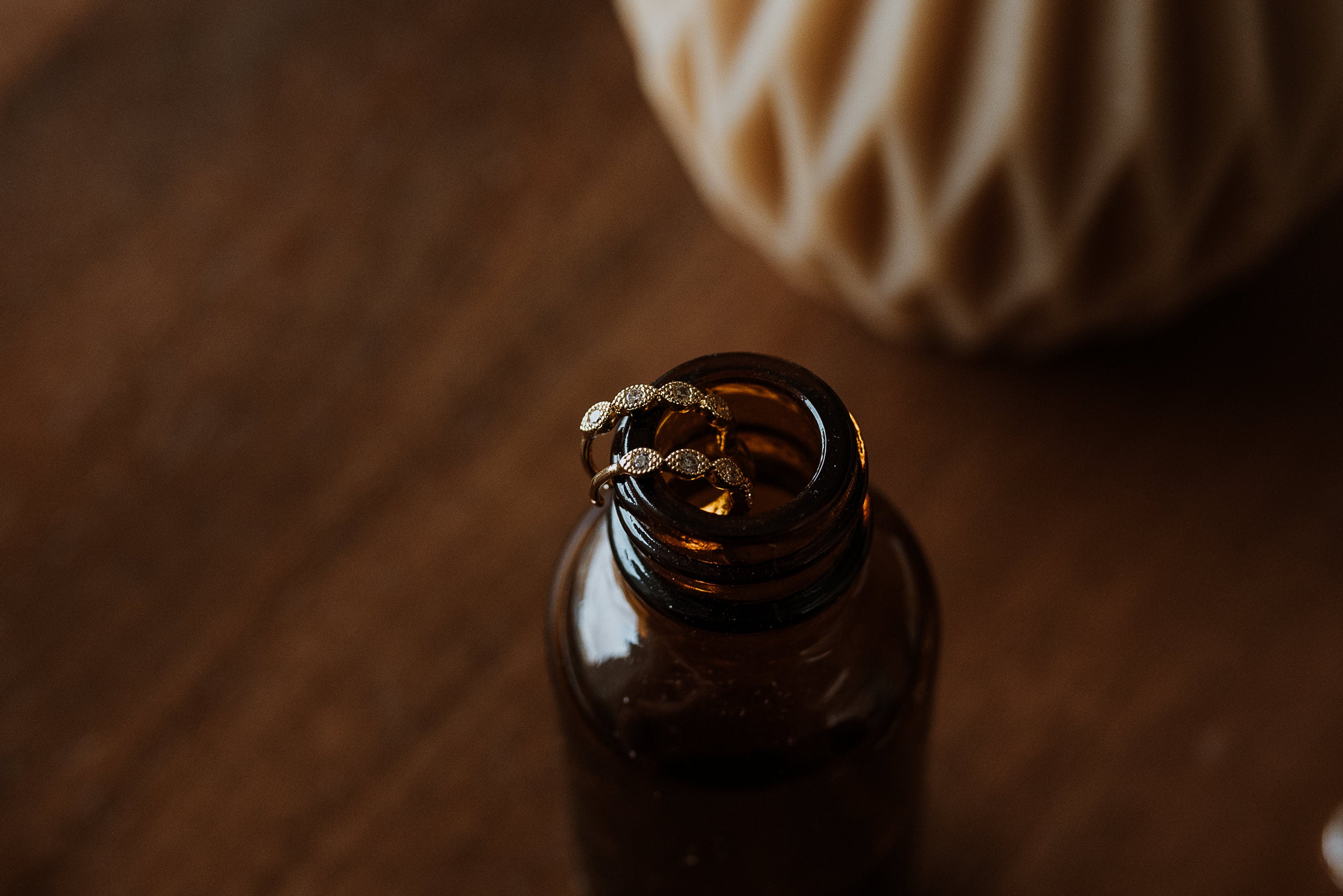 Brown glass bottle with hoop earrings on a wooden surface