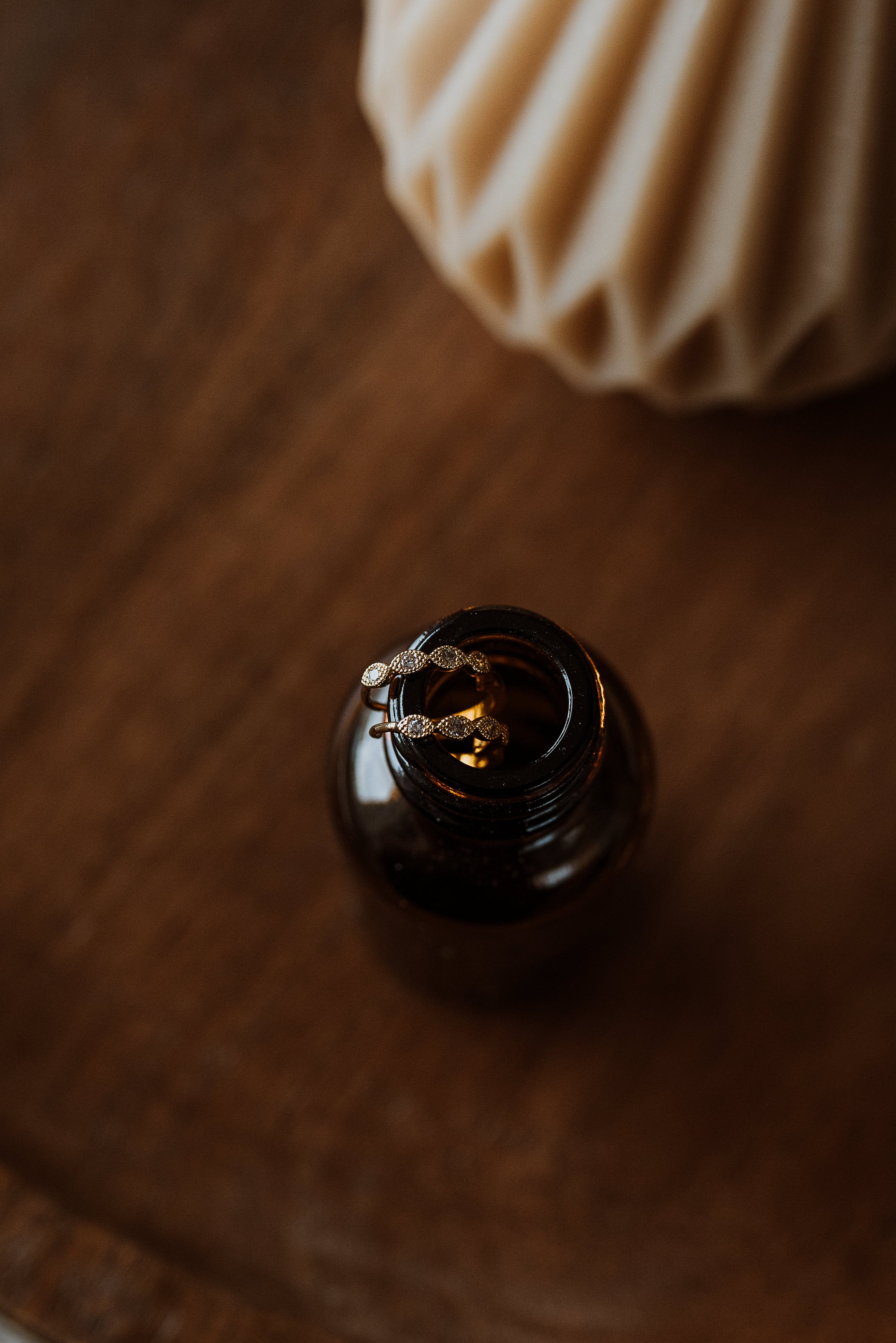 Close-up of a dark brown bottle with hoop earrings on a wooden surface.