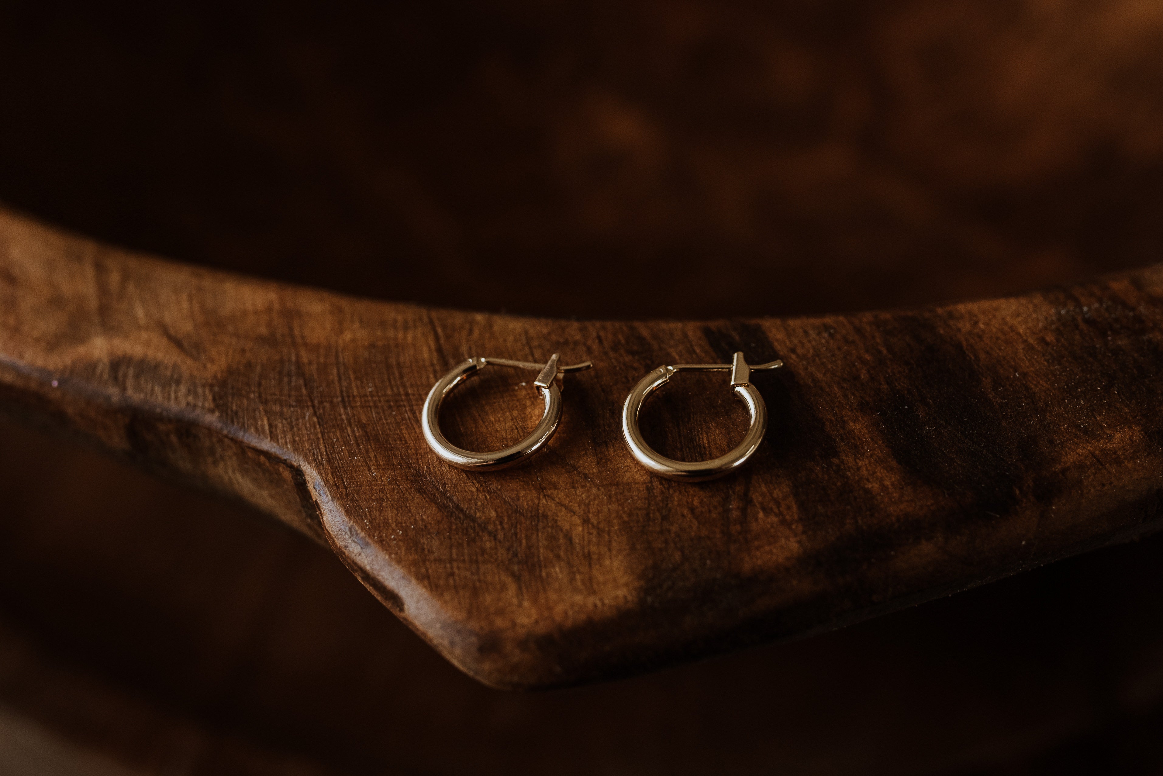 Two gold hoop earrings on a wooden surface with a dark background