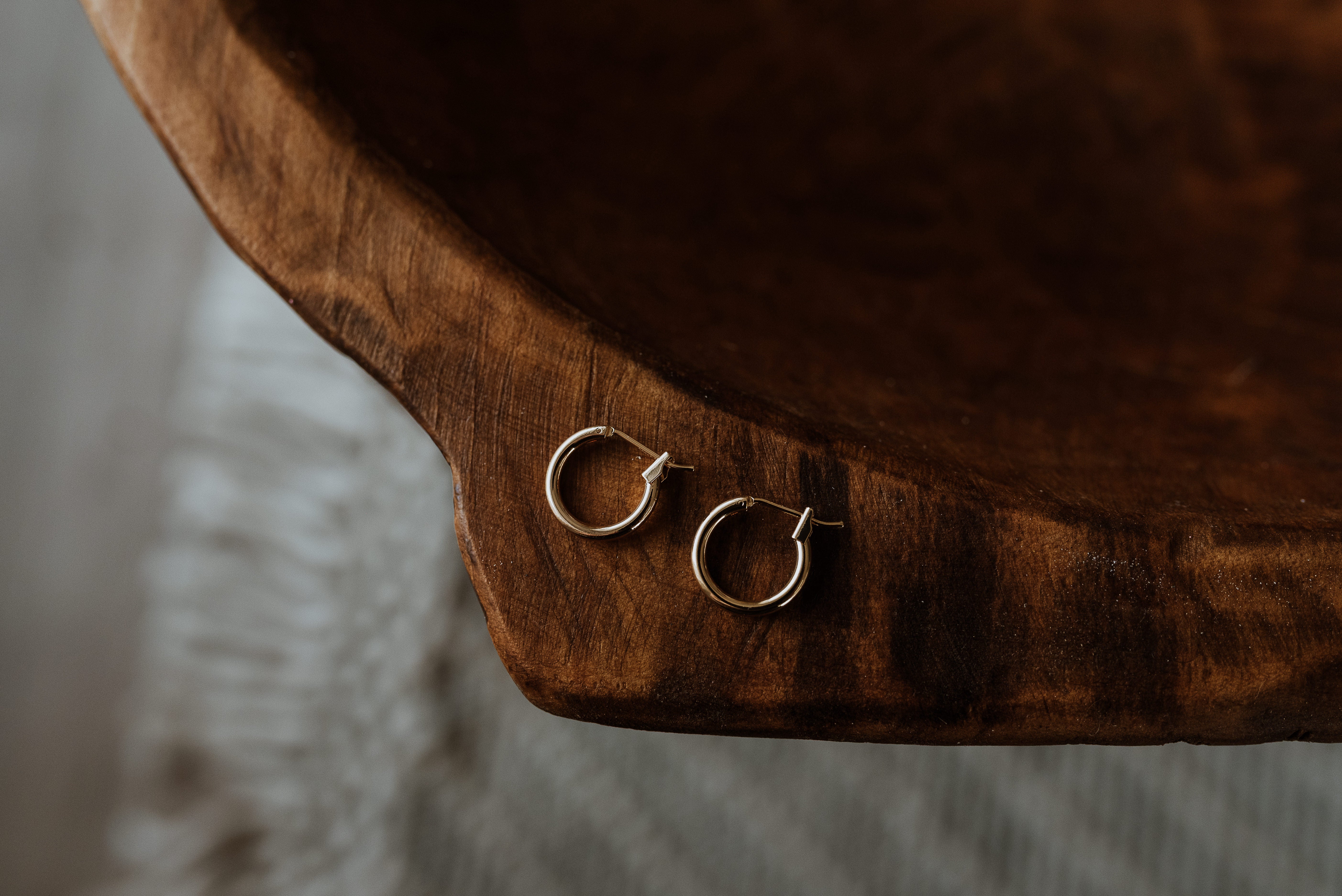 Two gold hoop earrings on a wooden surface with a blurred background