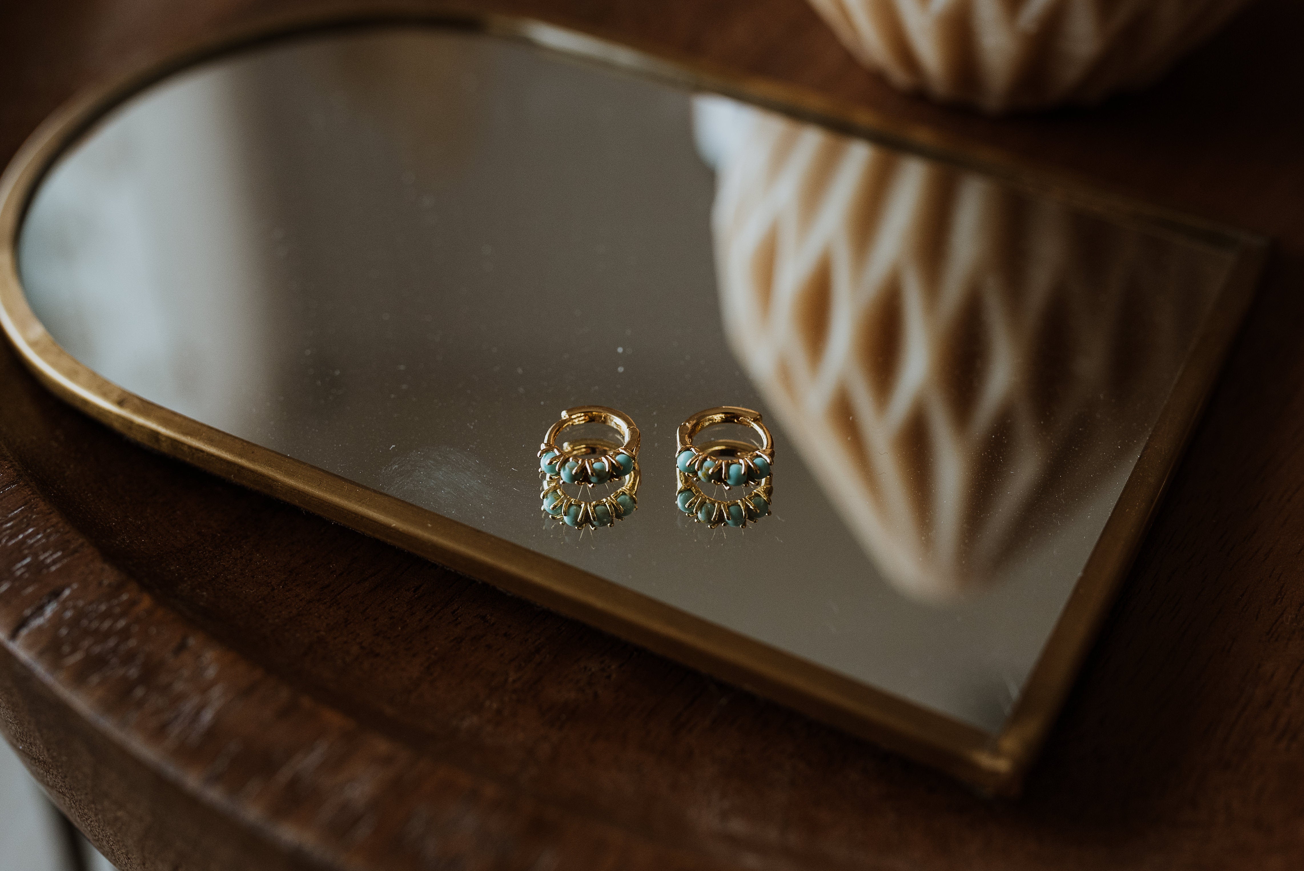 Gold earrings with turquoise stones on a reflective surface