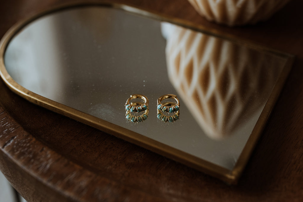 Gold earrings with turquoise stones on a reflective surface