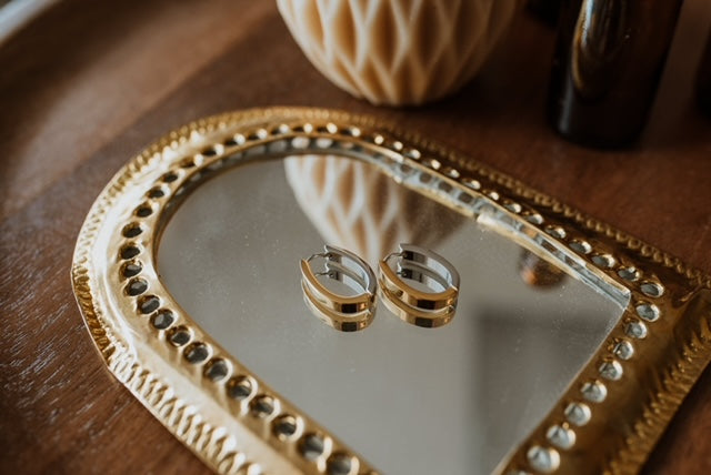 Gold hoop earrings on a mirrored gold arch-shaped tray with a blurred background