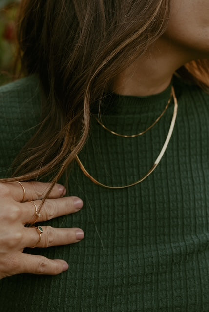Close-up of a person wearing gold necklaces and rings on a green background